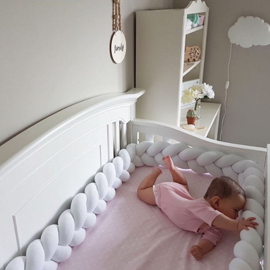 Bébé éveillé allongé sur le ventre, front et main posés sur un tour de lit tressé blanc en coton doux