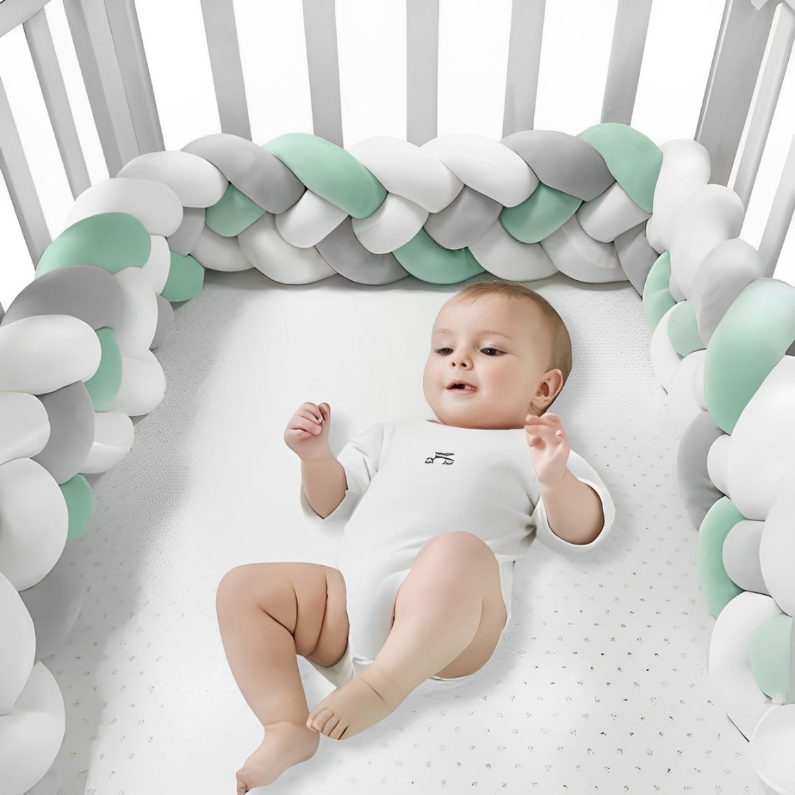 Bébé souriant allongé dans un lit avec tour de lit tressé 4 brins vert, blanc et gris, protection rembourrée contre les chocs et les coincements