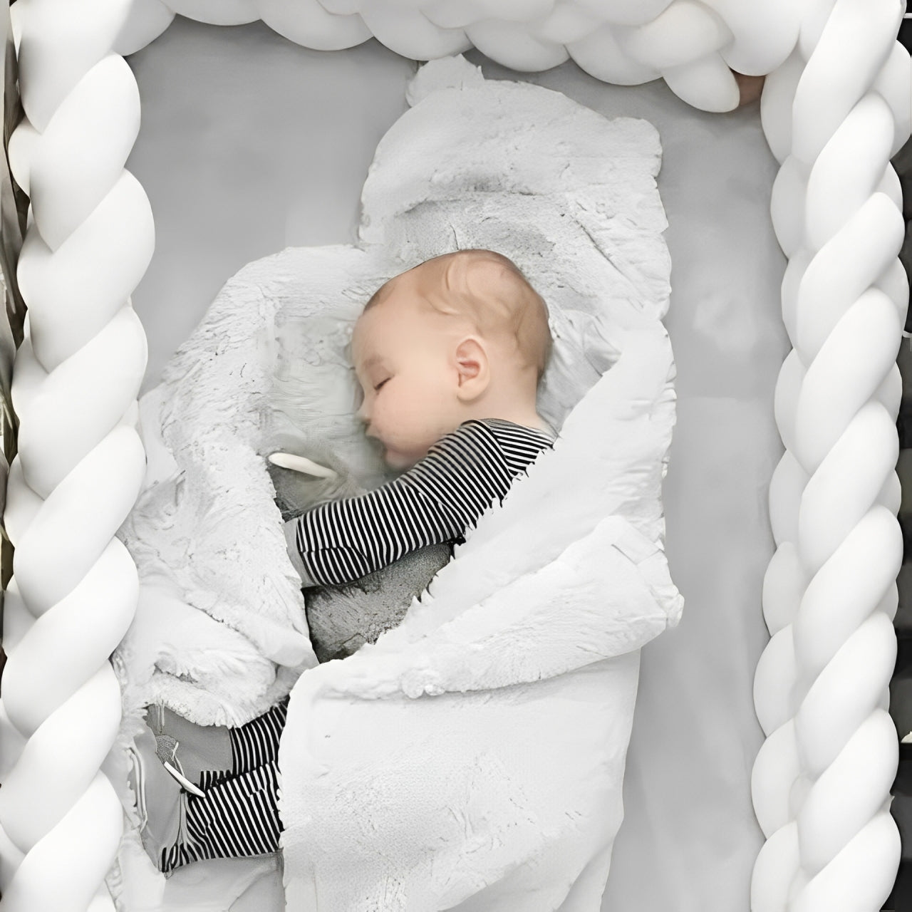Bébé endormi sur le côté dans un lit à barreaux sécurisé par un tour de lit tressé blanc