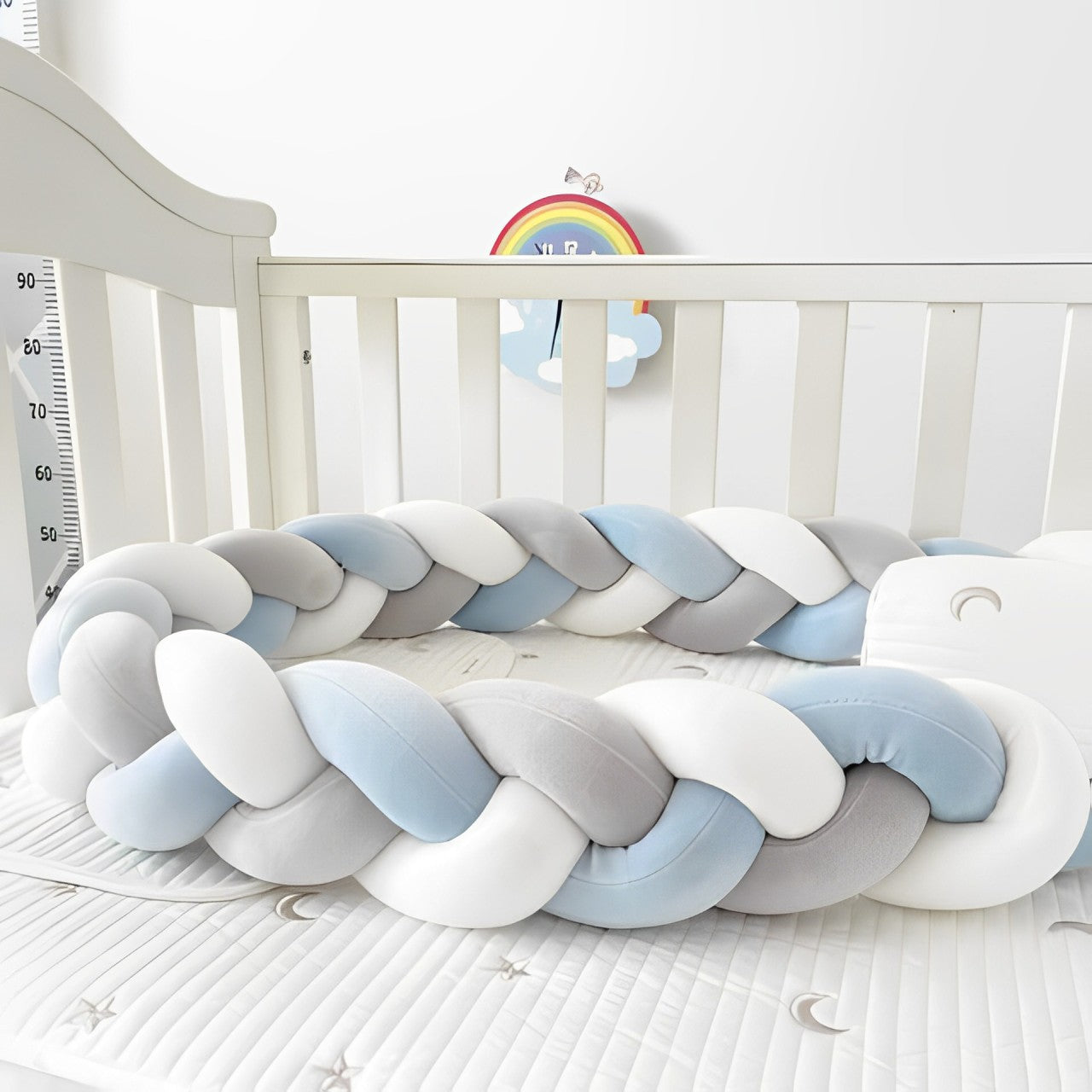 Tresse de lit, bleu, blanc et gris posée au centre d’un lit à barreaux pour bébé, vue en gros plan