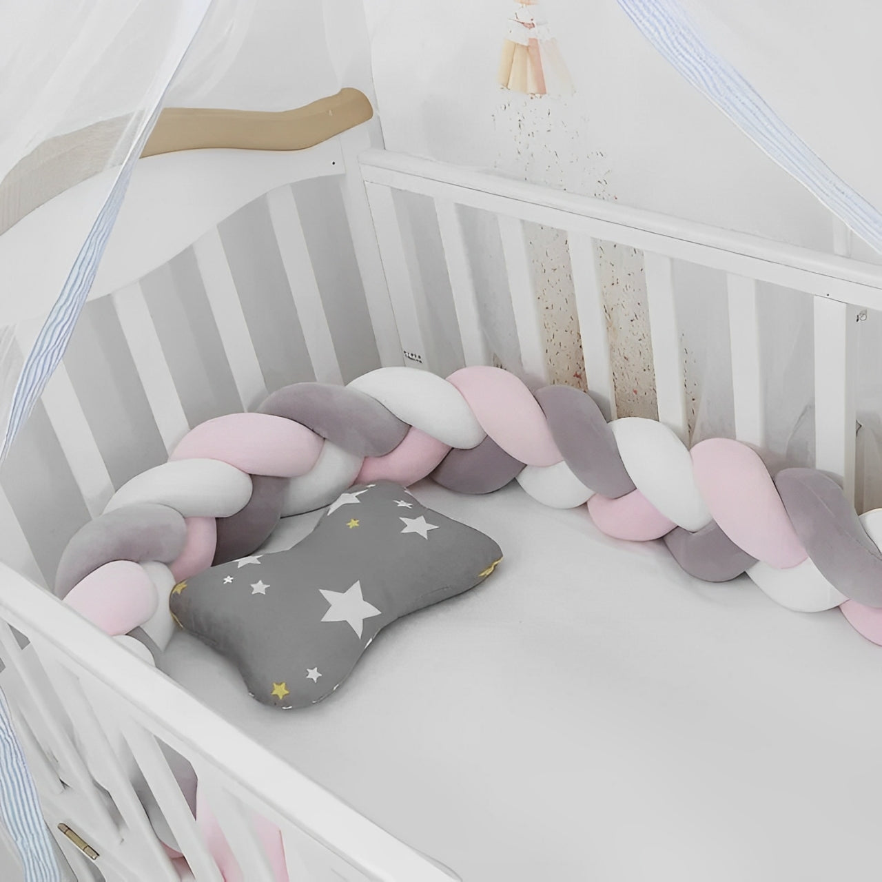 Une tresse de lit 3 brins, rose, gris, blanc respirante et douce qui sécurise un lit à barreaux pour bébé.