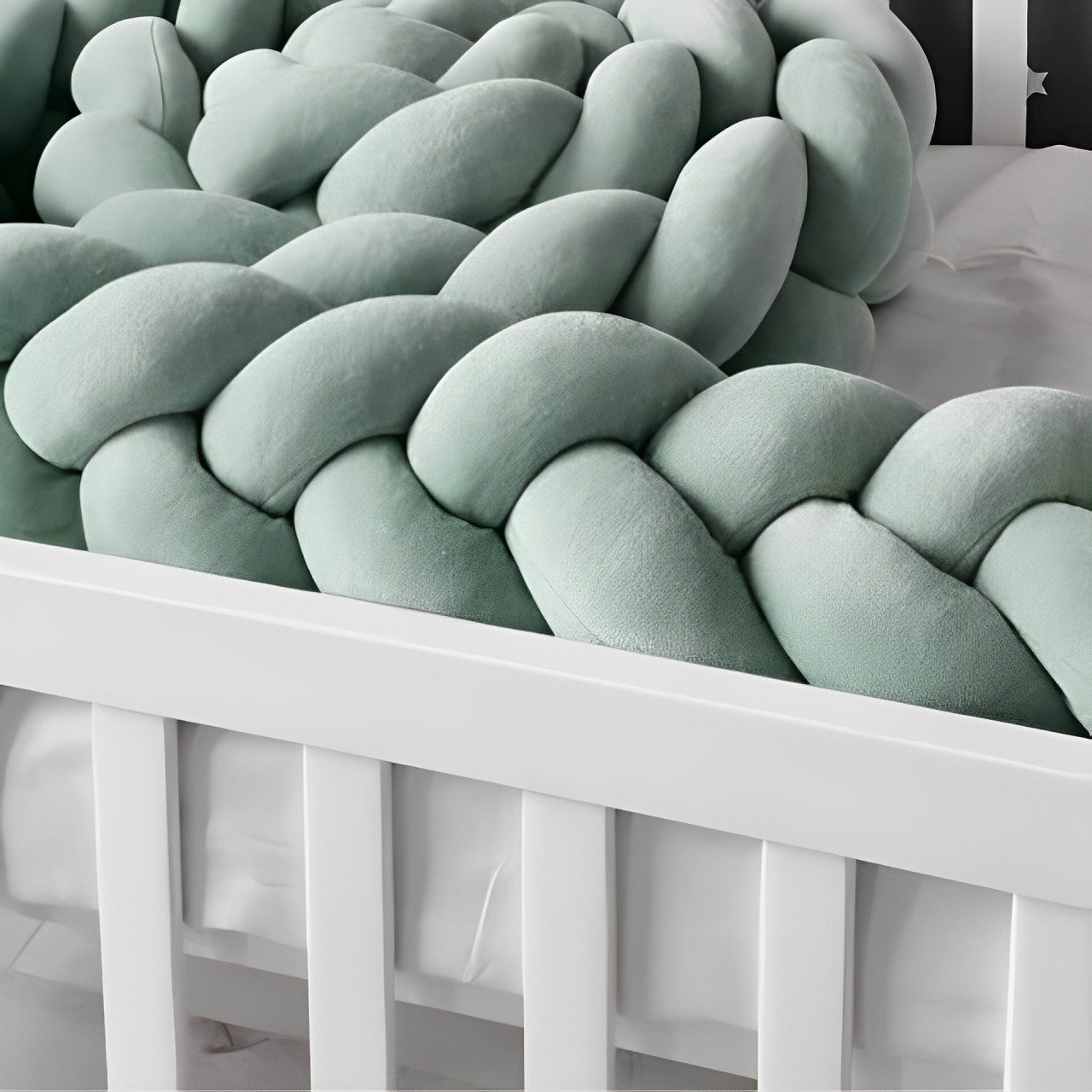 Vue rapprochée d’une tresse de lit vert sauge installée dans un lit à barreaux, idéale pour le confort de bébé.