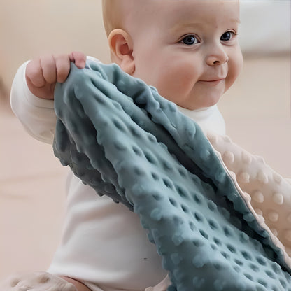 Bébé jouant avec une couverture bebe bicolore beige et bleu
