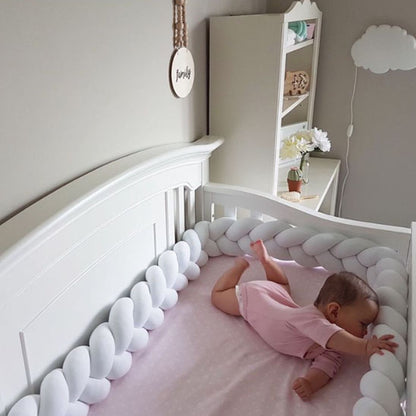 Bébé éveillé allongé sur le ventre, front et main posés sur un tour de lit tressé blanc en coton doux