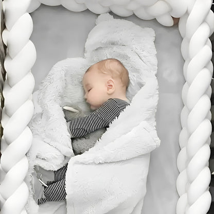 Bébé endormi sur le côté dans un lit à barreaux sécurisé par un tour de lit tressé blanc