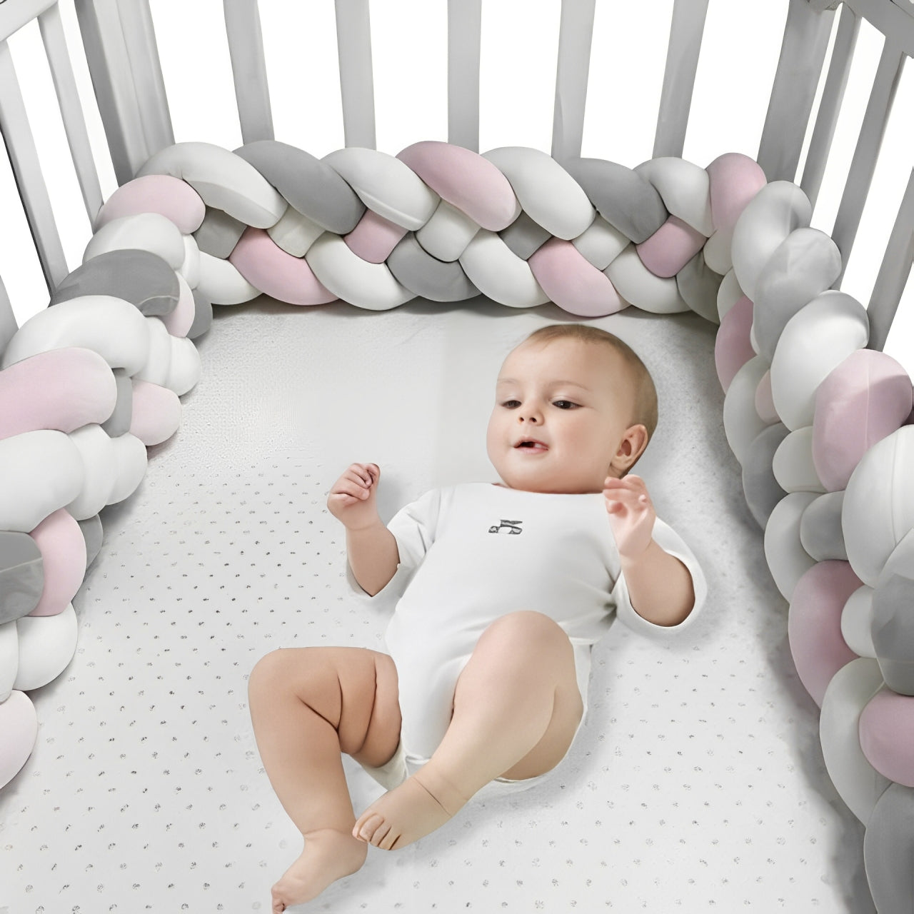 Tour de lit tressé rose, blanc et gris protégeant les barreaux du lit bébé